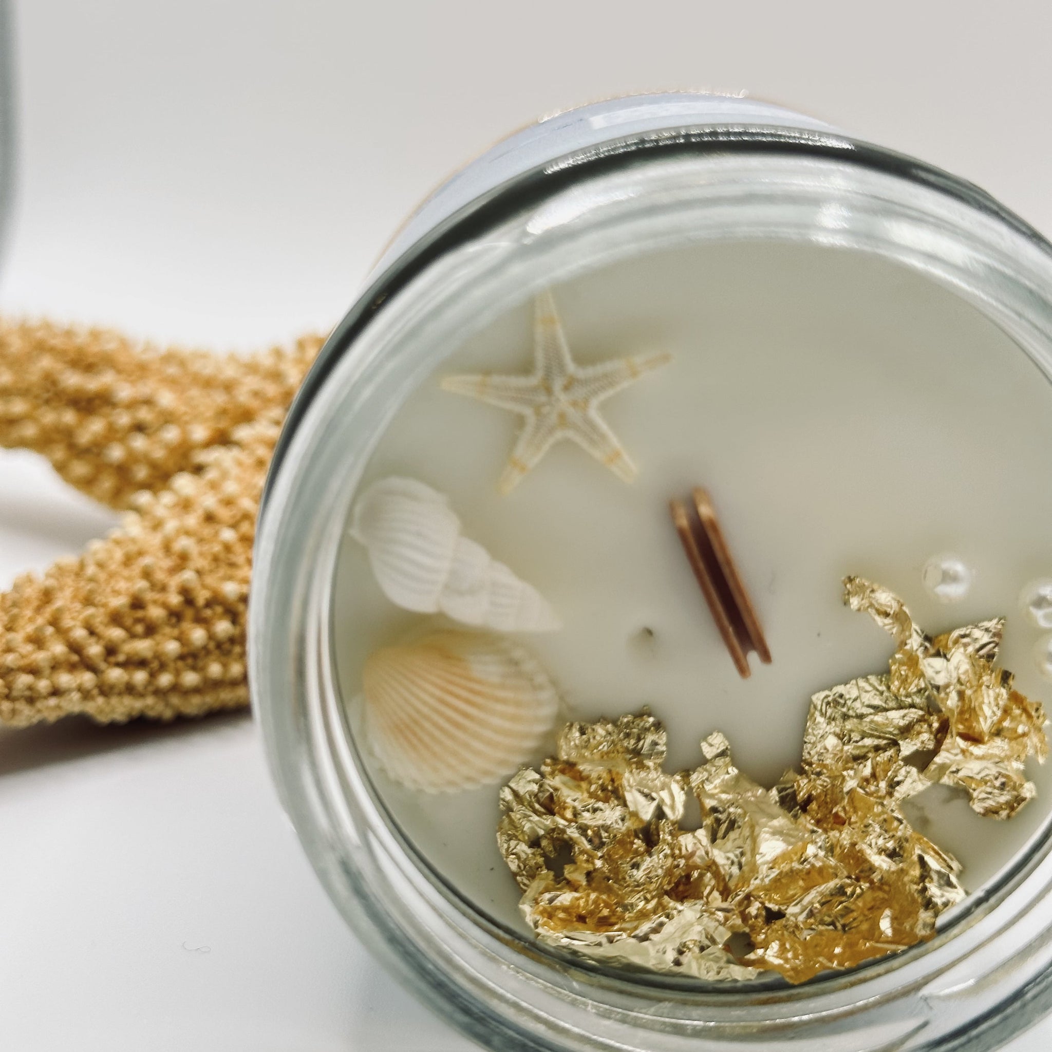 Plan haut de la bougie Émergence montrant les décorations de feuilles d’or, coquillages, perles et étoile de mer